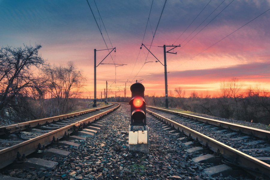Railway station with semaphore against sunny sky with clouds at sunset. Colorful industrial landscape. Railroad. Railway platform with traffic light in the evening. Heavy industry. Cargo shipping