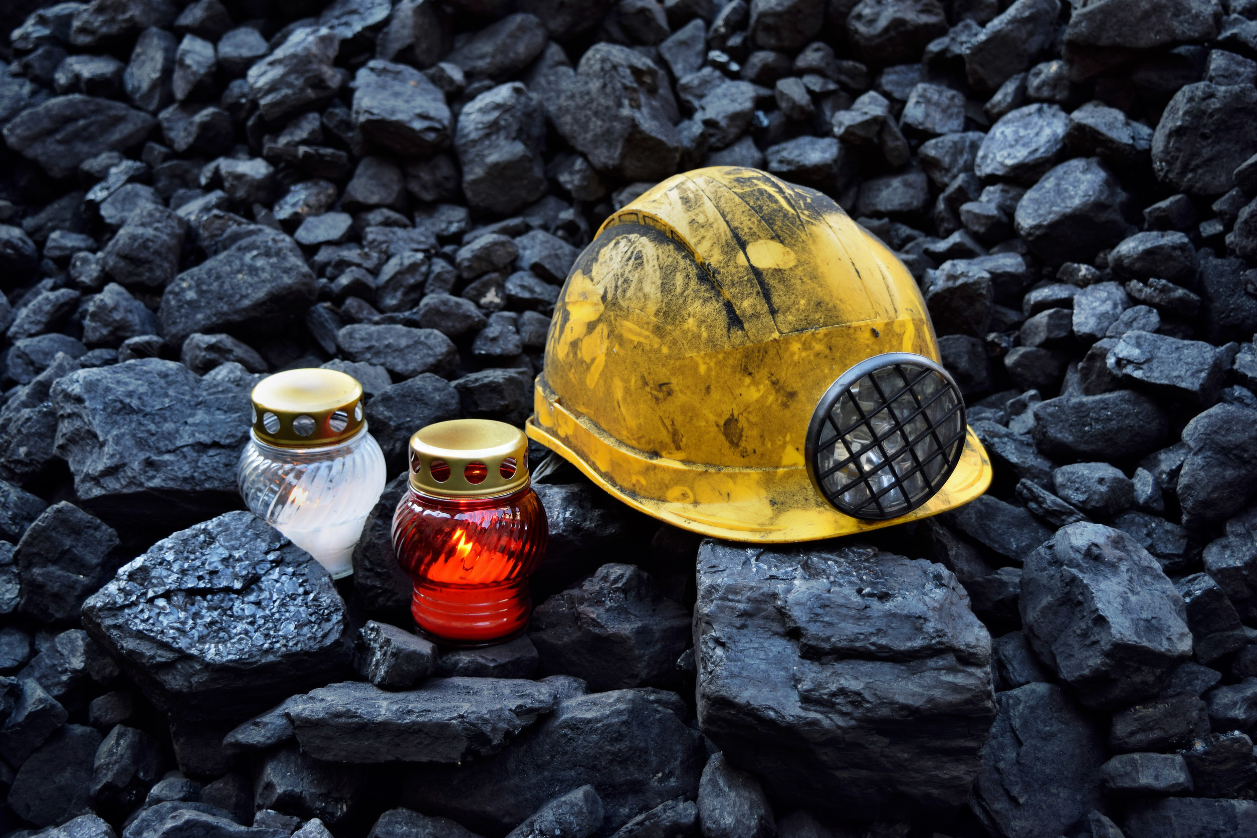 Lighted vigil light candle with mining helmet on cheap of coal after the fatal accident in the mine